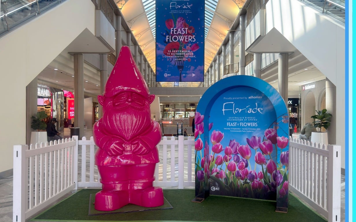 Floyd the large pink gnome next to a blue floriade pop up archway in centre court at Canberra Centre