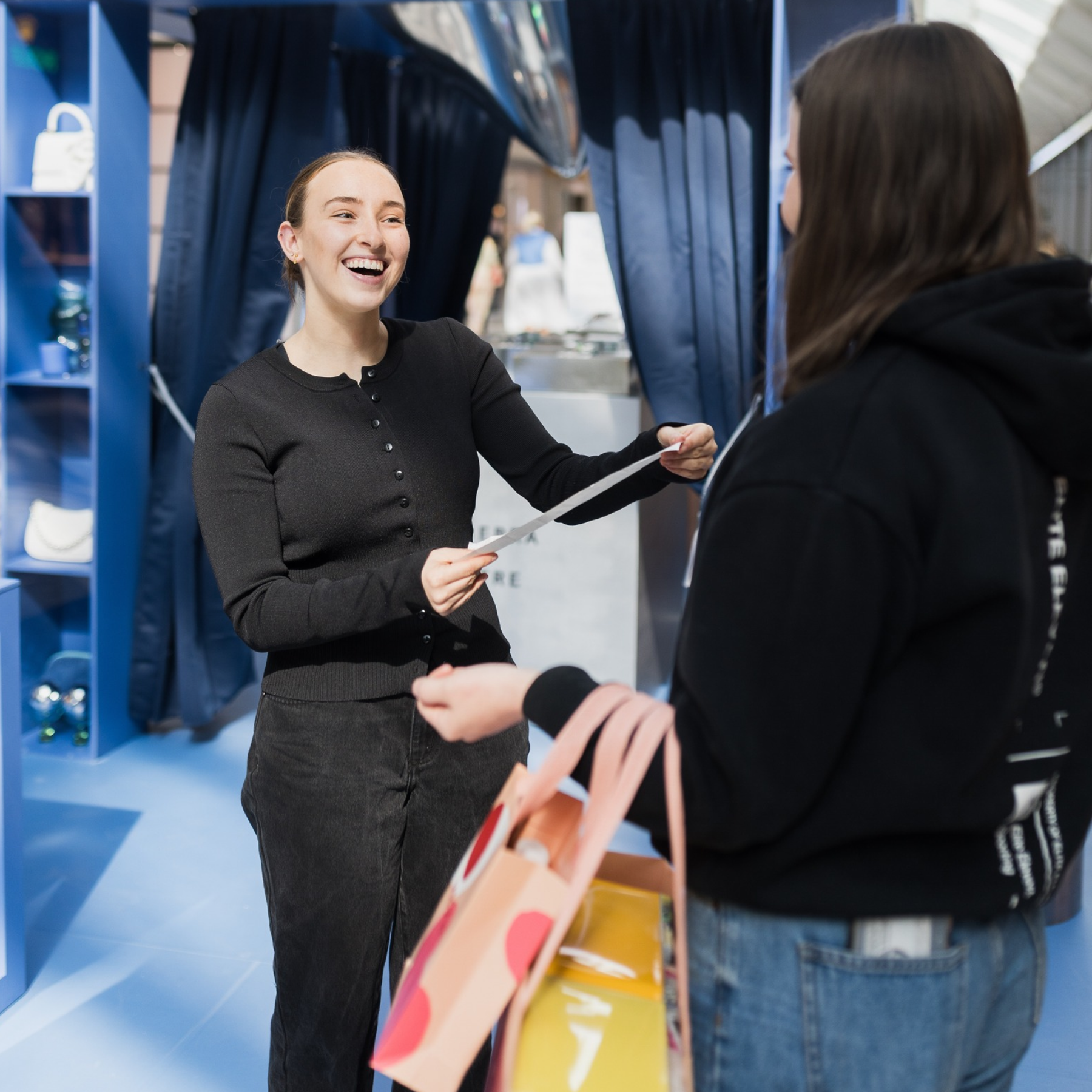 Image of a customer handing over a receipt while holding shopping bags at the Spend to Win pop-up.
